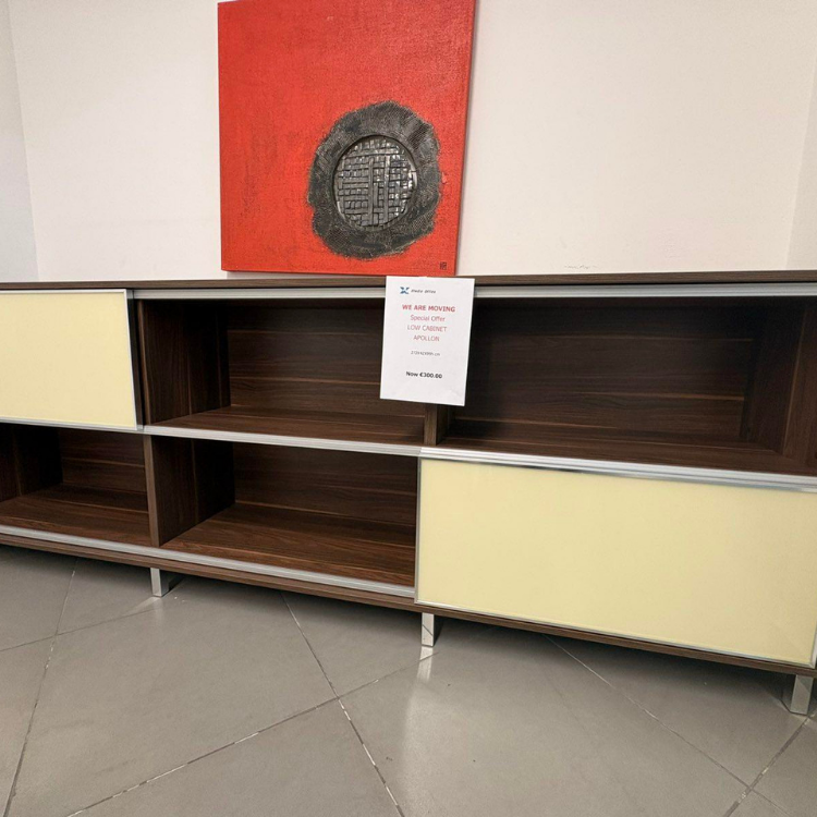 A low cabinet with a dark wood finish and light yellow doors is displayed against a white wall with a red painting.