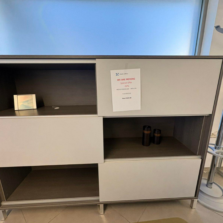 A grey and white shelving unit with open compartments and a sign attached to the upper right section.