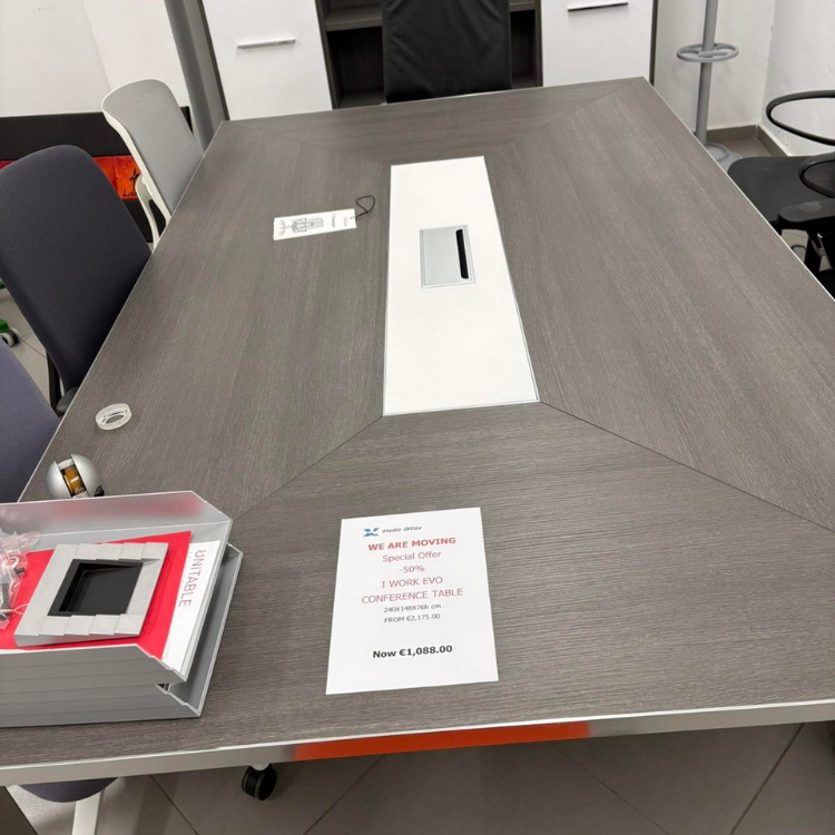 A large, gray, wooden conference table with a white center panel and visible chairs around it.