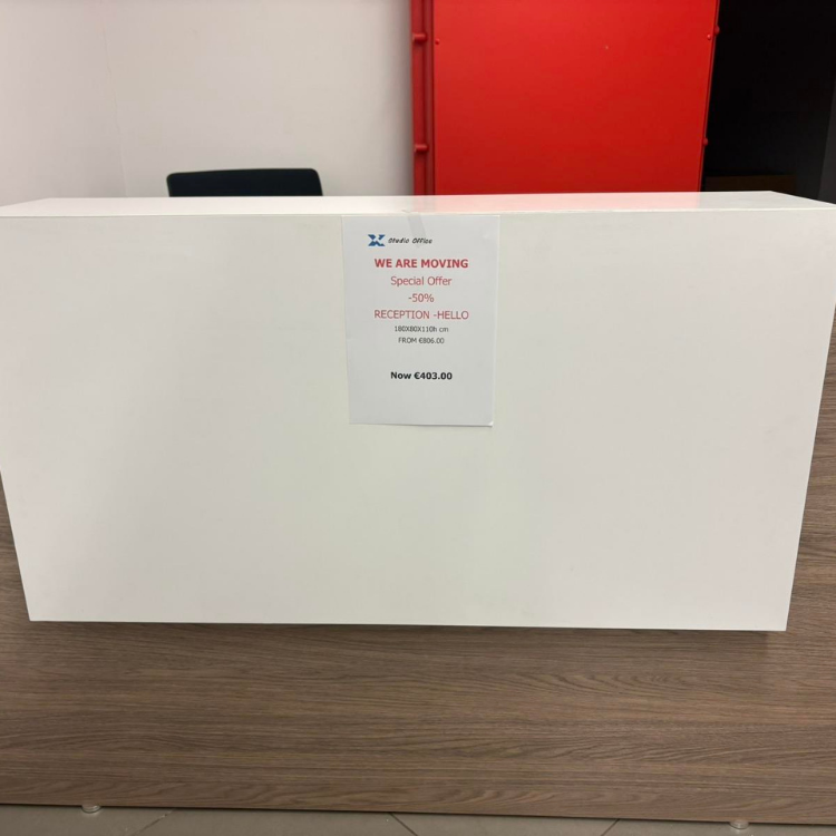 A white reception desk sits on a wood-look base, with a promotional sign attached to the front.