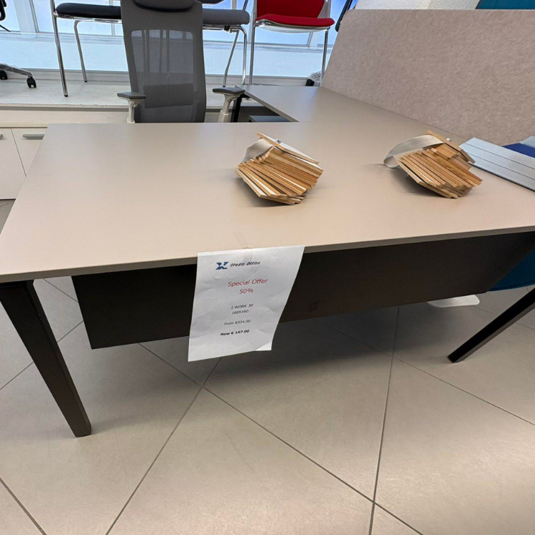 A desk with a light-colored top, dark brown accents, and two stacks of samples on top, with a sale sign attached.