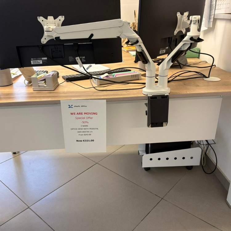 A desk with two monitors mounted on white adjustable arms, and a white sign displaying a moving announcement.