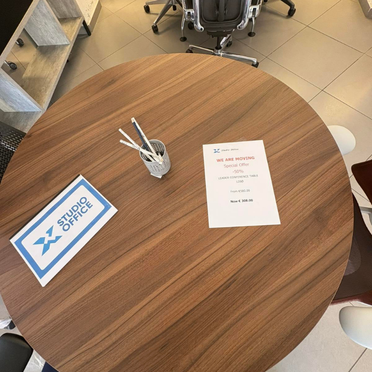 A round, wooden table with a pen holder, a promotional flyer, and a Studio Office card on top.