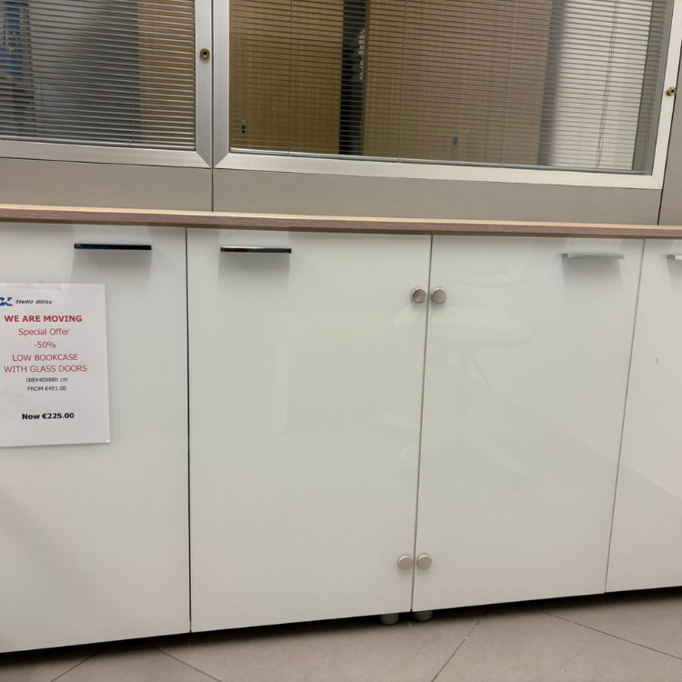 A white, modern cabinet with a light wood countertop sits beneath a window with closed blinds.