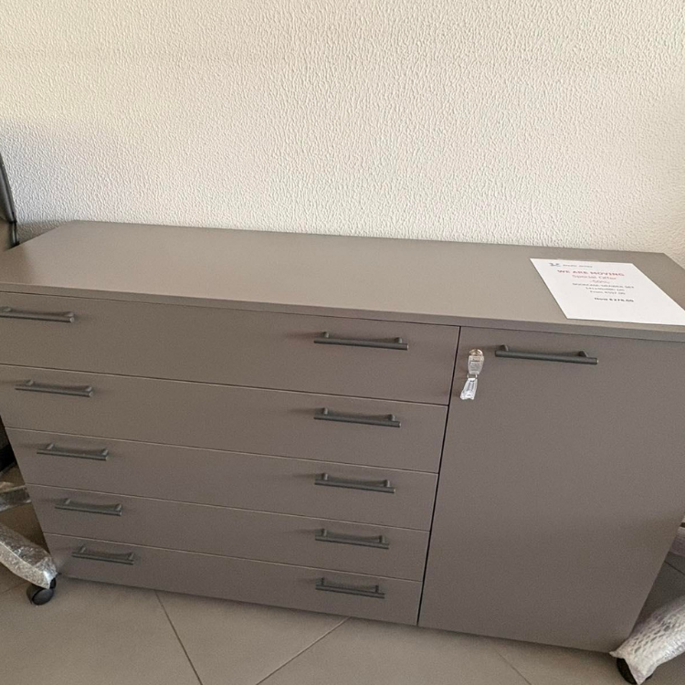A gray dresser with five drawers and a cabinet is positioned against a neutral-colored wall.