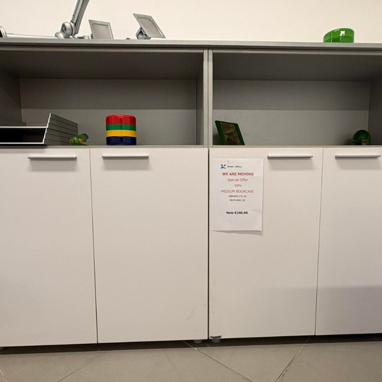 В белом шкафу с полками выставлены декоративные предметы; с правой стороны шкафа прикреплена рекламная вывеска.