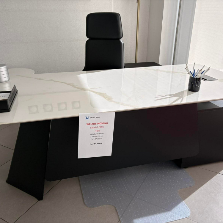 A modern office setup features a white marble-patterned desk with black accents and a black leather office chair.
