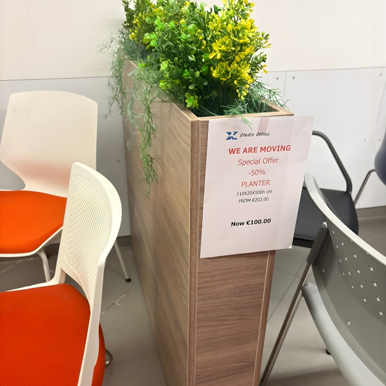 A tall, rectangular wooden planter with green and yellow plants, surrounded by office chairs.