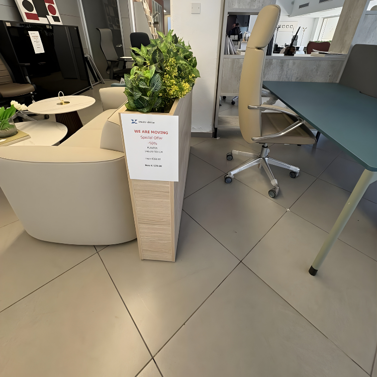 A showroom featuring office furniture including a desk, a light beige office chair, and a planter with green plants.