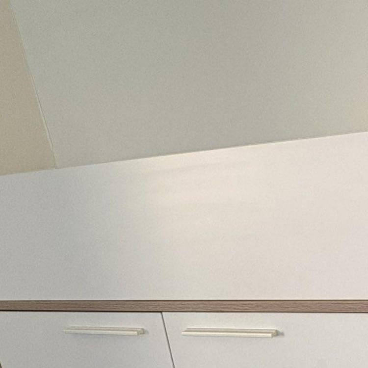 Close-up of white cabinets with light wood trim and simple, horizontal handles against a white wall and ceiling.