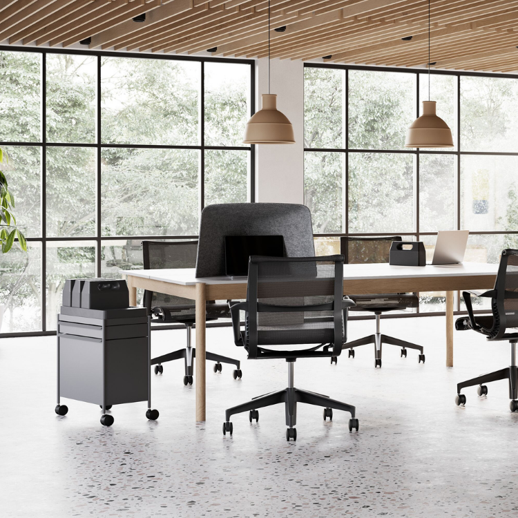 A long communal office table with fabric privacy dividers and rolling metal storage units in a bright workspace.