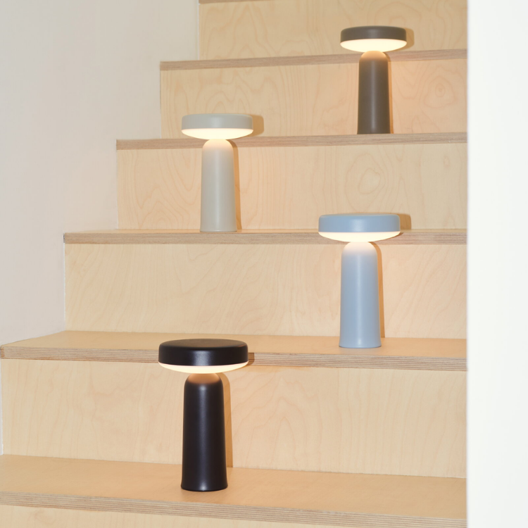 Four colorful portable lamps with tiered, plate-like heads are arranged on individual steps of a light wood staircase.