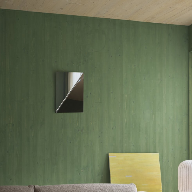 A rectangular mirror hangs on a green wood-paneled wall above a sofa, with a yellow abstract painting leaning below it.
